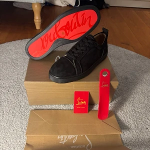 Svarta Christian Louboutin sneakers - Snygga svarta sneakers från Christian Louboutin i mocka med klassisk röd sula och svarta snören. Skorna har en låg profil och diskreta detaljer, perfekt för dig som vill sticka ut med exklusiv stil. Kommer med originalkartong och tillbehör.