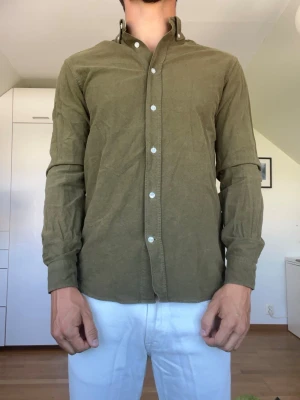 Olivgrön skjorta - Olivgrön skjorta från These Glory Days i strl S. Skjortan är tillverkad i 100% bomull. Inga defekter. Modellen är 178 cm och väger 77 kg. Hör gärna av dig vid frågor!