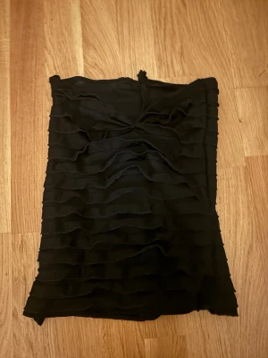 Svart tubtop  - Snygg svart axelbandslös kortklänning med volangdetaljer i lager på hela klänningen. Klänningen har en tight passform och är perfekt för dig som vill sticka ut med en stilren look. Materialet känns mjukt och följsamt mot kroppen. Om du intreserad jag vill bara förvarana att dom här byxorna är från en liten företag som hetter jennifer.