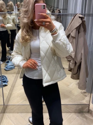 Vit quiltad pufferjacka - Säljer en snygg vit pufferjacka med quiltat mönster och dragkedja framtill. Jackan har ribbade muddar vid ärmsluten och en kort, boxig passform som ger en trendig look. Perfekt för kalla dagar och enkel att matcha med olika outfits. Från hm