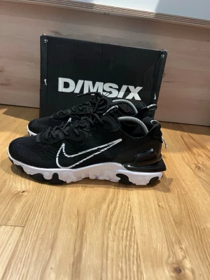 Nike react vision  - Snygga Nike D/MS/X sneakers i svart mesh med vit sula och vit swoosh-logga på sidan. Skorna har en chunky sula med svartvita detaljer och svarta skosnören. Perfekta för dig som gillar sportig och modern stil. 