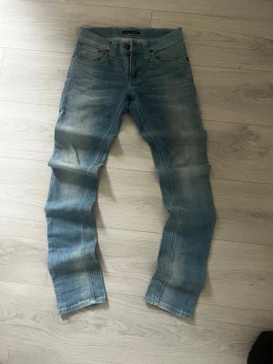Jean Nudie 👖 - Light blue wash Nudie Jeans, crafted from 100% organic cotton, featuring a classic skinny/slim fit. These jeans display natural fading and creasing consistent with wear, giving them a lived-in aesthetic.  ⭐️ Condition : 7/10 (Minor signs of wear, light creasing and fading) 🎲 Size : W26 L32 🎨 Color : Light Blue 📦 Fast and careful shipping
