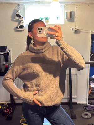 Beige polotröja i mjukt material - Mysig beige stickad polotröja med oversized passform och långa ärmar. Tröjan har en hög, bred polokrage och är gjord i ett fluffigt, mjukt material som känns skönt mot huden. Perfekt för kalla dagar och enkel att matcha med jeans eller kjol. Men passar även L!