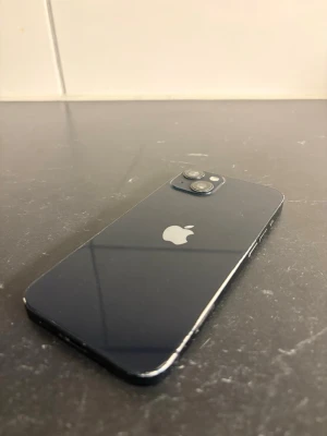 Mörkblå iPhone med dubbla kameror - Tjenare, finns bara en skada och de är på överglasset på bak kameran och så finns de lite repor här och där med inget allvarligt men den har tappat lite färg på ena sidan annars är de en Snygg mörkblå iPhone med stilren design och två kameror på baksidan. Telefonen har en platt glasbaksida och metallram, samt den klassiska Apple-loggan i mitten. Perfekt för dig som gillar modern teknik och vill ha en mobil med premiumkänsla.