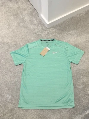 Mintgrön träningströja från Nike - Snygg mintgrön träningströja från Nike med korta ärmar och rund hals. Tillverkad i ett lätt och snabbtorkande material som passar perfekt för träning. Diskret Nike-logga på bröstet. Enkel och stilren design.