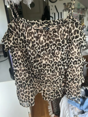 Leopardmönstrad volangtop med smala band - Säljer en leopardmönstrad topp med flera lager volanger och smala axelband. Toppen har en luftig och flowy passform, perfekt för dig som vill sticka ut. Materialet känns lätt och svalt, och mönstret är i beige och bruna toner.