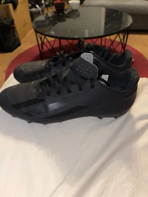 Svarta Adidas fotbollsskor - Säljer ett par helsvarta fotbollsskor från Adidas med klassisk låg profil och snörning. Skorna har diskreta svarta stripes på sidan och är tillverkade i syntetmaterial med dobbar för bra grepp på planen. Perfekta för dig som vill ha stilrena och funktionella skor till matchen.