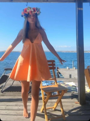 Kort orange sommarklänning - Säljer en söt kort klänning i ljus orange med tunna axelband och v-ringad urringning. Klänningen har en luftig passform och är perfekt för varma dagar. Materialet känns lätt och somrigt, och modellen ger en avslappnad vibe.