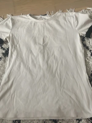 Vit basic t-shirt från Zara - En klassisk vit t-shirt från Zara i mjuk bomull. Enkel och stilren design med rund hals och korta ärmar. Perfekt att matcha med jeans eller shorts för en clean look.