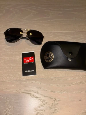 Ray-Ban svarta aviator solglasögon - Snygga aviator solglasögon från Ray-Ban med svarta glas och silverfärgade bågar. Klassisk pilotmodell som ger en cool vibe. Kommer med originalfodral och Ray-Ban-kort. Perfekta för soliga dagar och stilrena outfits.