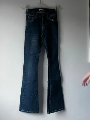 Mörkblå bootcut jeans - Säljer ett par mörkblå bootcut jeans med klassisk femficksmodell och normal midja. Jeansen har en lätt utsvängd passform nedtill och är tillverkade i ett mjukt denimtyg. 