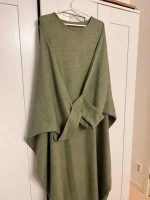 Grön abaya - Grön butterfly abaya I mjukt linen material, färgen kan avvika lite från bilderna och verkligheten. Strl XL, använd och slitaget syns på bilderna.