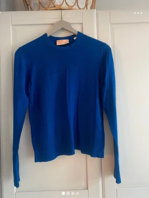 Kornblå tröja - En enkel och stilren kornblå tröja med rund halsringning och långa ärmar. Tröjan har en rak passform och är tillverkad i ett mjukt, tunt stickat material som passar perfekt till lager på lager. Strö L.