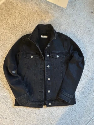 Svart jeansjacka från Gina Tricot - Snygg svart jeansjacka från Gina Tricot med klassisk krage, silverfärgade knappar och två bröstfickor med lock. 