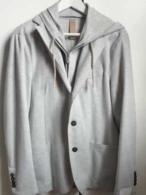 Riktigt lyxig blazer från eleventy Milano. - Sprillans ny eleventy kavaj-jacka, köpt från stenströms i Helsingborg, plagget är helt oanvänd och har fortfarande prislappen kvar. Jackan är en kombination av både uppklätt och avslappnat vilket skapar en unik stil som sticker ut bland mängden. Plagget är i gjort av bland de finaste materialen på marknaden direkt från Italien vilket skapar en mycket bra passform. Produktbeskrivningen hittar ni på sista bilden i annonsen där plagget beskrivs mer och dess material. (Avtagbar innerjacka med huva).