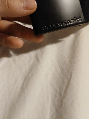 Svart tygbälte från Bluewear - Snyggt svart tygbälte från Bluewear med stilren metallspänne. Bältet har en enkel och clean design som passar till många olika outfits. Perfekt för dig som gillar en minimalistisk look och vill ha ett bälte som är lätt att justera. Priset kan diskuteras.