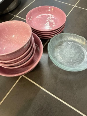 Rosa skålar och assietter i glas - Säljer ett set med rosa skålar och assietter i keramik med vita prickar och blommönster samt två små assietter i genomskinligt glas med blommig struktur. Perfekt för servering av snacks eller dessert.