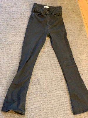 Svarta bootcut jeans med hög midja - Säljer ett par svarta bootcut jeans med hög midja och klassisk femficksdesign. Jeansen har utsvängda ben och är tillverkade i ett stretchigt denimtyg som sitter snyggt. Perfekta för dig som gillar en retroinspirerad look.
