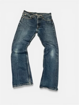Levi's 555 - Klassiska blå jeans från Levi's med rak passform och fem fickor. Jeansen har slitningar och ljusare partier för en vintage look. Tillverkade i robust denim med detaljer som nitar och läderpatch bak i midjan.