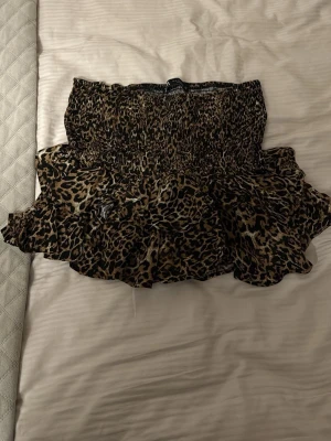 Leopardmönstrad volangkjol från Zara - Kort kjol från Zara med leopardmönster och volangdetaljer. Kjolen har smock i midjan för en bekväm passform och är tillverkad i ett lätt, flödande material. Perfekt för dig som vill sticka ut med en trendig look.