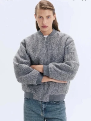 Grå bomberjacka i teddy från HM - Snygg grå bomberjacka i teddy-material från HM. Jackan har dragkedja framtill, ribbade muddar vid ärmslut och midja samt fickor på sidorna och en ärmficka med dragkedja. Perfekt för en trendig och avslappnad look.