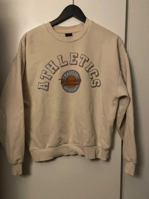 Beige sweatshirt med Athletics-tryck - Säljer en beige sweatshirt från Ginatricot. Tröjan har ribbade muddar vid ärmslut och nederkant. Okej skick! Pris kan diskuteras 🩷