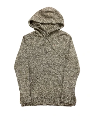 Gråmelerad hoodie från Hollister - Mysig gråmelerad hoodie från Hollister med dragsko i huvan och liten logga på bröstet. Stickad känsla i materialet och klassisk känguruficka framtill. Perfekt för en avslappnad och stilren look.