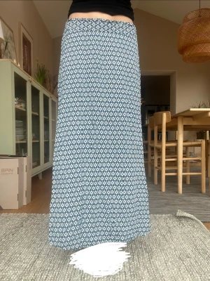 Blåvit långkjol med grafiskt mönster - Säljer en blåvit långkjol med grafiskt mönster. Kjolen har en rak och flowy passform. Perfekt för dig som gillar en avslappnad men ändå stilren look. Materialet känns mjukt. Lite kort på mig är 167.