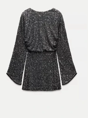 Svart glittrig klänning med vida ärmar - Supersnygg svart klänning med glittriga paljetter över hela plagget. Klänningen har vida långärmar och en draperad, öppen rygg. Säljs inte på hemsidan längre 🤍 helt nytt med prislapp kvar 