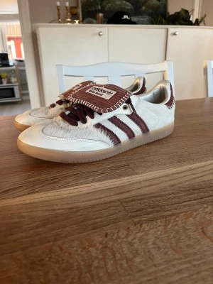 Adidas Samba x Wales Bonner vita sneakers - Unika Adidas Samba x Wales Bonner sneakers i vitt med vinröda detaljer och klassiska tre ränder. Ovandelen är i hårig mocka/läder med kontrastsömmar och gummisula. Tungan är extra lång och har Wales Bonner branding. Pris ej hugget i sten vid snabb affär!