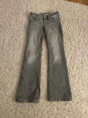 Grå bootcut jeans med slitningar - Säljer ett par grå bootcut jeans med snygga slitningar framtill och bakfickor med broderade detaljer. Jeansen har klassisk femficksmodell och normal midja. Perfekta för dig som gillar en avslappnad men trendig look.