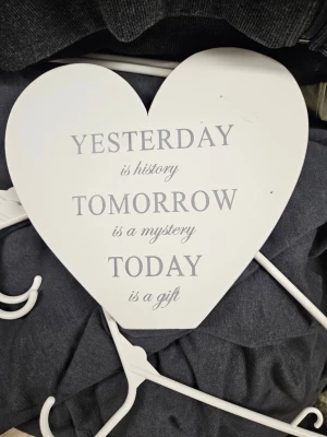 Vitt hjärtformat väggord i trä - Dekorativt hjärtformat väggord i vitt trä med texten 'Yesterday is history, Tomorrow is a mystery, Today is a gift' i grå stilren font. Perfekt som inredningsdetalj för att skapa en inspirerande känsla i rummet.