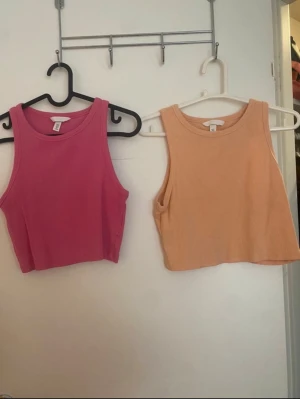 Två croppade ribbade linnen H&M - Säljer två croppade linnen från H&M, ett i rosa och ett i ljus orange. Båda är ribbade och ärmlösa med rund halsringning. Perfekta till sommaren och superenkla att matcha med jeans eller kjol.