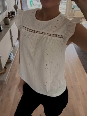 Vit och mörkblå blus med spetsdetaljer - Söt vit blus med broderade hålmönster och spetsdetalj över bröstet. Blusen har volangärmar och rund halsringning. Säljer även den mörkblåa som är exakt lika dan! 