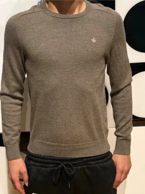 Beige stickad Morris tröja - Snygg beige stickad tröja med rund hals och diskret emblem på bröstet. Tröjan har långa ärmar och ribbade muddar vid ärmslut och nederkant. Perfekt för dig som gillar en stilren och enkel look. Obs inte jag som tagit bilderna förra ägaren som tagit bilderna, inte använd sen dess. Priset kan absolut diskuteras. 1799kr ny kan sitta tight om du är över 170