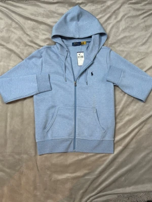 Ljusblå hoodie från Polo Ralph Lauren - Snygg ljusblå hoodie från Polo Ralph Lauren med dragkedja. Helt ny med lapparna kvar. Skit snygg färg nu till vår o sommaren. Köpt på hedefashion outlet för 1835kr (outlet lapp som syns över orginal lapp.)