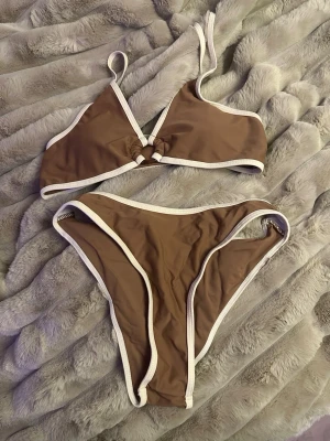 Tre trendiga bikinis i brunt, orange och vitt!  - Säljer tre snygga bikinis! En brun bikini med vita kanter och ringdetalj framtill, samt en orange och vit mönstrad trekantsbikini med knyt i sidorna och nacken. Samt en vit bikini med en strandkjol! Perfekta för sommaren och strandhäng! Säljer alla tre separat också, mer information om alla tre bikinis finns på deras separata annonser! Men hit kommer du om du vill köpa alla tre för ett bättre pris! Alla bikinis är i Storlek S! 