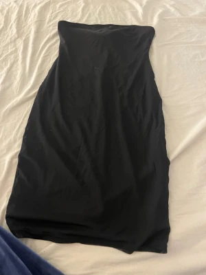 Svart axelbandslös klänning Forever 21 - Säljer en svart, axelbandslös klänning från Forever 21. Klänningen har en enkel och stilren design med rak passform och är tillverkad i ett mjukt syntetmaterial. Perfekt för dig som gillar minimalistisk stil.