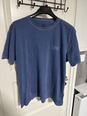 Blå t-shirt från Lee - Snygg blå t-shirt från Lee med diskret logga på bröstet. Klassisk rund halsringning och korta ärmar. Tillverkad i mjuk bomull som känns skön mot huden. Perfekt till jeans eller shorts för en avslappnad look.