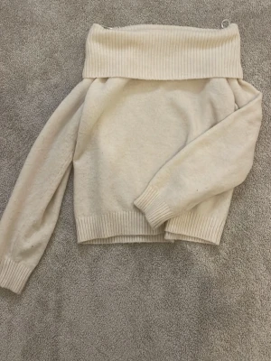 Offshoulder stickad tröja H&M - Krämvit stickad offshoulder-tröja från H&M med bred ribbad kant upptill och vid ärmslut samt nederkant. Mjuk och skön, perfekt för lager på lager och en avslappnad men trendig look. Storlek 158/164