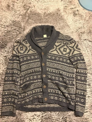 Grå cardigan med mönster från Hollister - Hollister Mysig grå kofta med beige mönster och sjalkrage. Koftan har träknappar framtill och två fickor. Stickad i mjukt material och har långa ärmar. Perfekt för lager på lager och ger en avslappnad men snygg look.