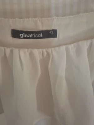 Vit offshoulder blus Gina Tricot - Säljer en vit offshoulder blus från Gina Tricot i storlek 42. Blusen har volangdetaljer upptill och är tillverkad i ett tunt, lätt och något transparent tyg som ger ett luftigt intryck. Perfekt för en trendig och avslappnad look.