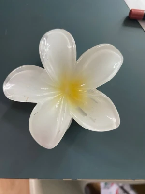 Vit blomformad hårklämma - Säljer en söt hårklämma i form av en blomma med vita och gula toner. Klämman är gjord i plast och har en tydlig blomdesign som ger en fräsch och somrig känsla till din look. Perfekt för att piffa upp frisyren med en unik accessoar.