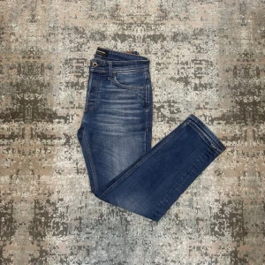 Blåa jeans från Jack & Jones - Snygga blåa jeans från Jack & Jones med klassisk femficksdesign och guldfärgade sömmar. Jeansen har en lätt tvättad look med subtila slitningar och normalhög midja. Perfekta för en avslappnad och trendig stil. Endast använd fåtal gånger! Skicket ser ut o va ny!