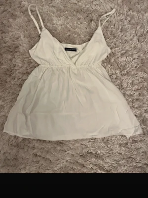 Brandy melville top - Säljer en vit linnetopp från Brandy melville med omlott-design och tunna justerbara axelband. Toppen har en luftig passform och v-ringad fram. Perfekt för varma dagar och enkel att matcha med jeans eller kjol. One size och aldrig använd 