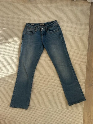 Blå bootcut jeans från LTB- valerie - Säljer ett par klassiska blå bootcut jeans från LTB, modell Valerie. Jeansen har fem fickor, normalhög midja och snygga slitningar framtill. Tillverkade i mjukt denimtyg som sitter skönt och ger en avslappnad look.