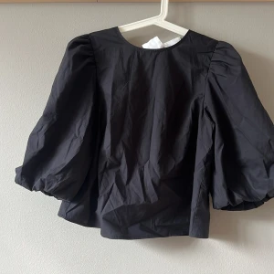 Trendig blus - Supersnygg svart blus från Divided med stora puffärmar och rund hals. Baksidan har vita knytband som ger en cool kontrast och unik look. Använd en gång!💕