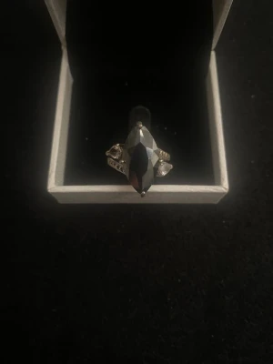 Silverring med svart sten - Snygg silverring med en stor, avlång svart sten i mitten och små klara stenar på sidorna. Ringen har en elegant och unik design som sticker ut. Perfekt accessoar för dig som gillar statement-smycken.