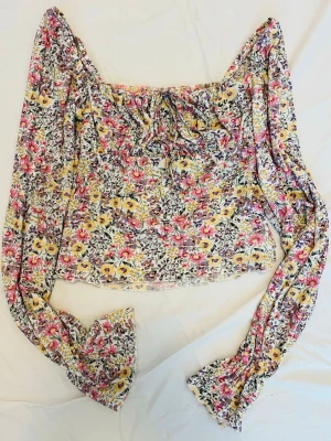 Blommig blus från Gina Tricot storlek xs - Supersöt blommig blus från Gina Tricot i storlek XS. Blusen har långa ärmar med volang vid ärmslut, smockad kropp och en söt knytning framtill. Färgerna går i vitt, rosa, gult och lila.