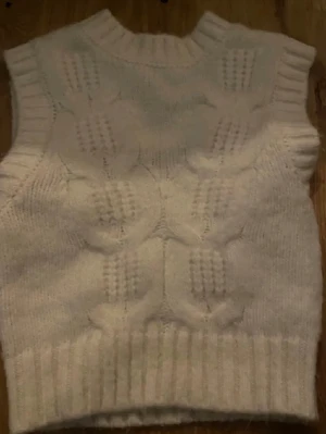 Vit stickad väst - Mysig vit stickad väst med grovt mönster och ribbad kant nertill. Perfekt att slänga över en skjorta eller t-shirt för en trendig lager-på-lager-look. 